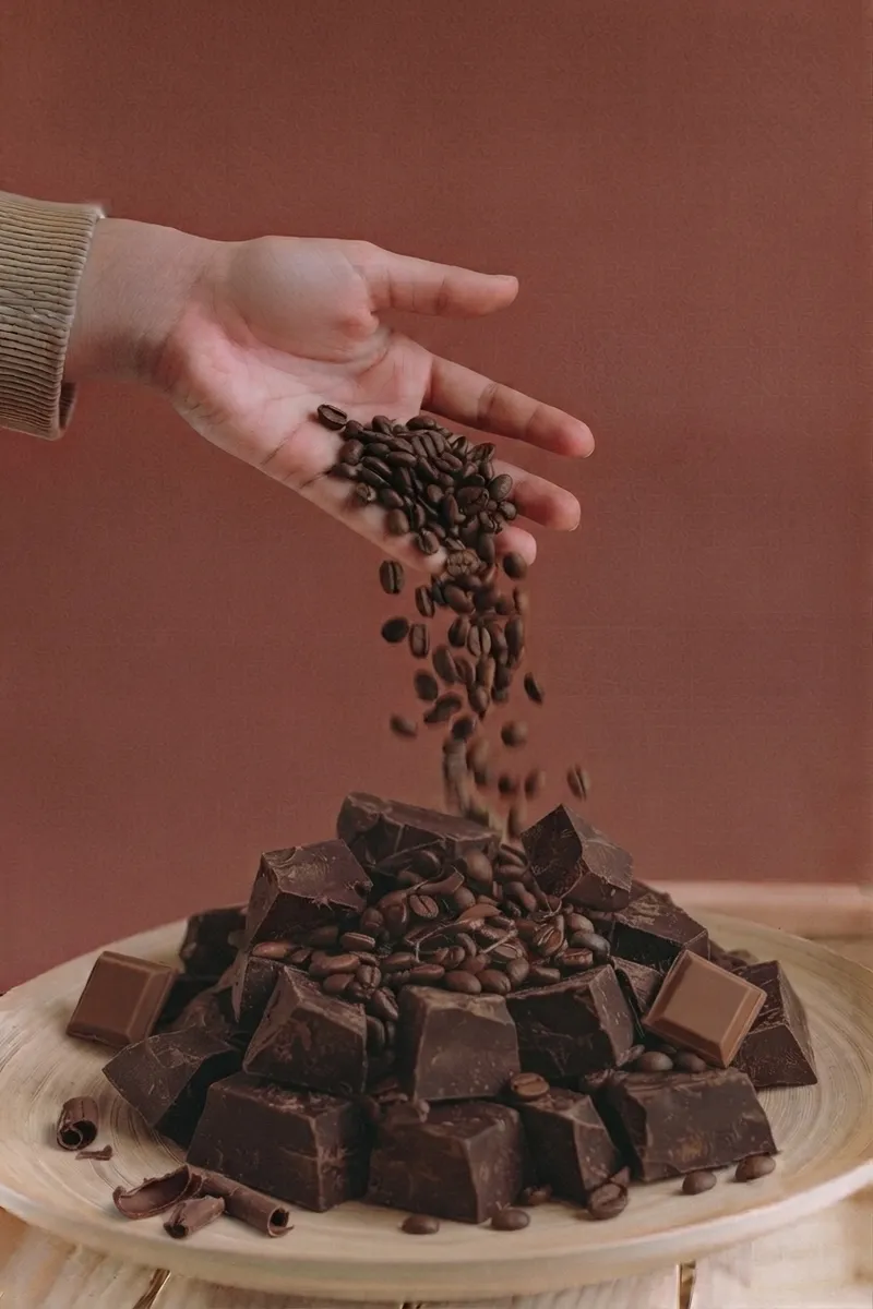 Hand pouring coffee beans over broken dark chocolate chunks
