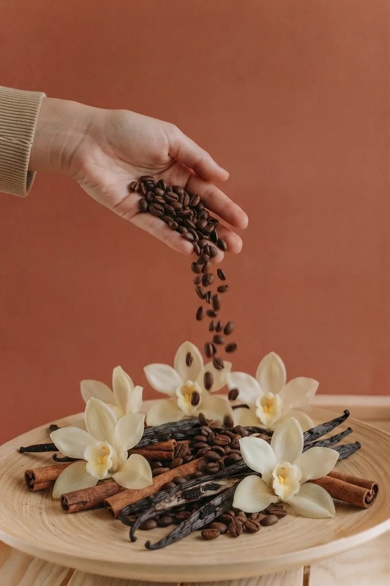 Hand pouring coffee beans over vanilla pods and orchid flowers