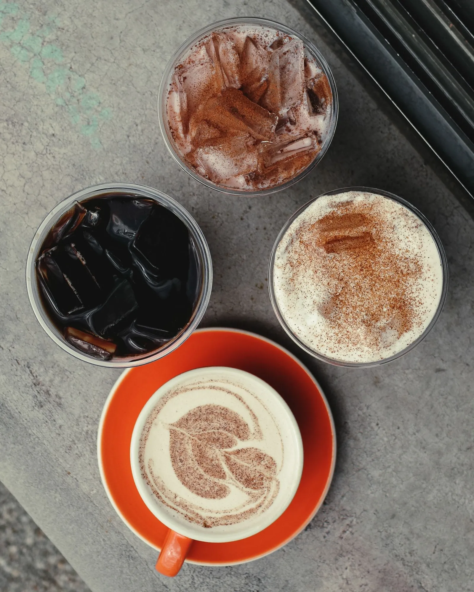 Four coffee drinks seen from above, one in an orange saucer
